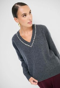 Maglione grigio con scollatura a V, decorato con strass a forma di ovale lungo il collo. Texture morbida con polsini e orlo a costine.