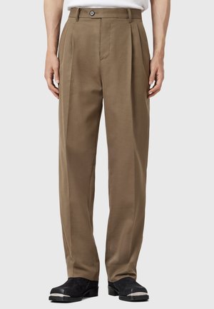 Brown pleated trousers with a straight cut, made of a smooth fabric. Features a button closure and belt loops, paired with black shoes.