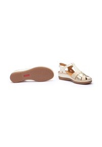 Sandale beige avec des détails tressés, ouverte à l'avant et avec des brides croisées. Dotée d'une semelle intérieure rembourrée et d'une semelle en caoutchouc texturé pour une meilleure adhérence.