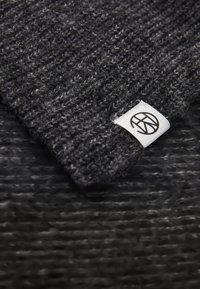 Black and gray knitted beanie with a textured pattern and a small white label featuring a circular logo sewn into the edge.