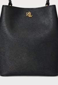Musta ämpärilaukku, joka on valmistettu teksturoidusta materiaalista ja jossa on kultainen logo etupuolella. Suunnittelu on yksinkertainen ja pinta on sileä.