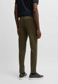 Olivgröna byxor i slim fit, tillverkade av ett mjukt tyg. Har två bakfickor, slät front och bärs med mörka sneakers.