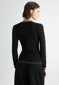 Getailleerde zwarte blouse met lange mouwen en een gestructureerde glans. Heeft een effen lichaam en een sprankelende rand aan de zoom en manchetten.
