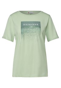 T-shirt en coton vert clair à manches courtes, présentant un graphique carré avec du texte bleu et blanc indiquant "HORAIRE DORÉ apercevez un rayon de soleil."