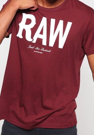 T-shirt à manches courtes bordeaux en coton avec le texte blanc "RAW" et le slogan "Just The Product". Design simple avec col rond.