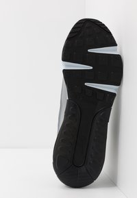 Träningsskor med en svart gummisula, grå mesh-övre del och vita detaljer. Har texturerad slitbana för grepp och dämpade designelement.