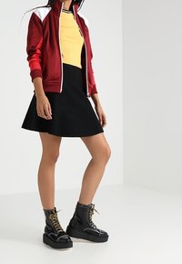 Red and white zip-up jacket over a yellow ribbed top, paired with a black skirt and black platform boots with gold laces and stitching details.
