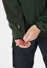 Veste softshell verte avec des poignets élastiques, fermeture éclair et logo "W PRO 8000" sur la manche. Texture lisse et design ajusté.