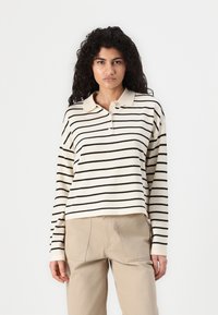 Cream and black striped long-sleeve polo shirt with a collar and two buttons, paired with beige pants featuring patch pockets.