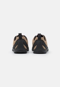 Deux paires de chaussures brunes et noires sont présentées de l'arrière sur un fond blanc uni, mettant en valeur leur design et leur structure.