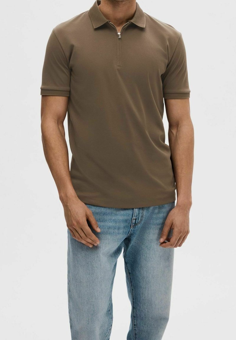 Brun polo t-shirt med dragkedja i kragen, korta ärmar och ribbade manschetter; kombinerad med ljusblå denimjeans. Slätt tyg med rak passform.