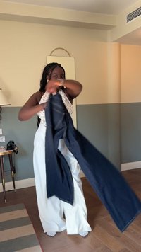 Tmavě modré džíny z denimu, které člověk drží v rukou. Mají design s pěti kapsami a kontrastním prošíváním, doplněné bílým vzorovaným topem.