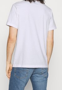 Vitt bomullströja med korta ärmar, rund hals och rak fåll, som bärs tillsammans med blå denimjeans med detaljer på bakfickorna.