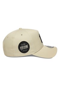 Beige Baseballkappe mit einem schwarzen kreisförmigen Logo, das den Text "New York Yankees" zeigt, strukturiertem Schirm und Belüftungsöffnungen oben.