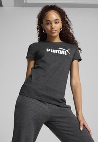 Grå T-shirt med korte ærmer, der har et stort hvidt "PUMA" logo foran. Glat bomuldsagtig tekstur, i kombination med matchende grå bukser.