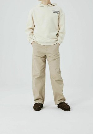 Hellbeige Kapuzenpullover mit Textdruck auf der Brust, kombiniert mit sandfarbenen Chinos und braunen Mokassins im Mokassinstil. Einfaches Design, lockere Passform, glatte Textur.