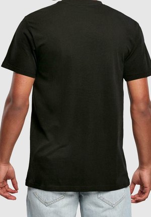 Mann in schlichtem schwarzen T-Shirt mit kurzen Ärmeln und hellblauer Jeans, von hinten vor einem schlichten grauen Hintergrund gezeigt.