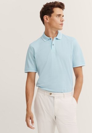 Himmelblaues Baumwoll-Poloshirt mit Kragen, zwei Knöpfen und gerippten Bündchen, kombiniert mit weißen Hosen mit Knopfdetails.