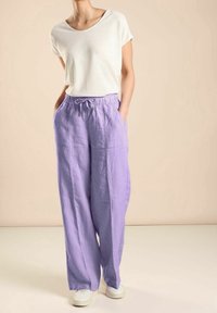 Lehký bílý top s krátkým rukávem, doplněný o volné lila lněné kalhoty s elastickým pasem a bočními kapsami. Svetlé obuv.