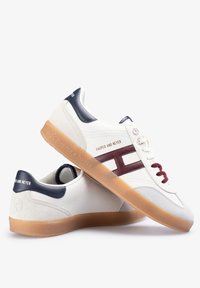 Zapatillas blancas con suela de goma, acentos color burdeos y detalles en azul marino. Presentan un upper de cuero liso y un panel de ante texturizado.