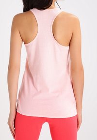 Top senza maniche di un rosa chiaro, realizzato in un tessuto testurizzato e traspirante, con design a schiena scoperta, abbinato a leggings di un rosa vivace.