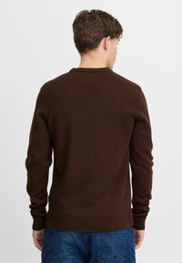 Brauner Strickpullover mit einem gerippten Rundhalsausschnitt, langen Ärmeln und einem engen Bund. Der Stoff hat eine glatte Textur und minimale Details.
