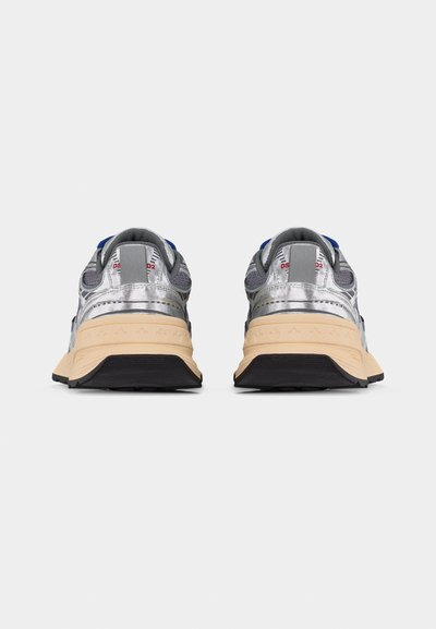 Ζευγάρι μεταλλικά ασημί αθλητικά παπούτσια με μπεζ μεσοπάτους και μαύρες εξωτερικές σόλες, από πίσω σε λευκό φόντο.