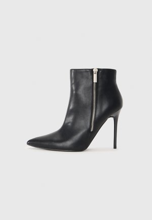 Bota de tornozelo em couro preto com bico afiado, salto agulha e detalhe de zíper prateado na lateral. Textura suave e design ajustado.
