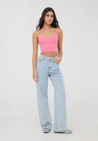 Top corto a coste di un brillante rosa fucsia con spalline sottili, abbinato a jeans a gamba larga di un blu chiaro con tasche frontali e un leggero effetto rovinato.