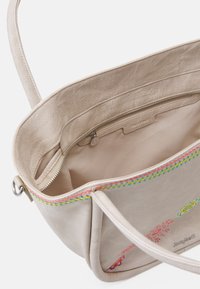 Beige læderhåndtaske med broderede blomsterdesigns, glat tekstur og en lynlåslomme indeni. Har farverig syning langs kanten.