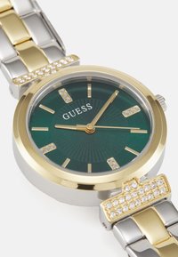 Orologio in metallo dorato e argentato con quadrante verde, tre lancette dorate e dettagli in cristallo sugli indicatori delle ore e sul bracciale. Design della cassa rotonda.