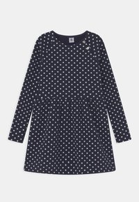 Marint blå långärmad klänning med vita prickar, med en rynkad midja och tryckknappar på axlarna, tillverkad av mjukt material.