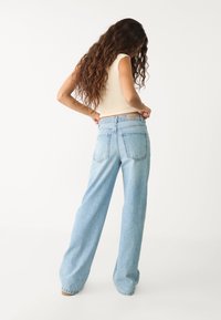 Vaqueros de pierna ancha en azul claro, confeccionados en denim, con una cintura alta, dos bolsillos traseros y efectos de desvanecimiento sutiles en toda la prenda.