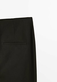 Pantalon noir sur mesure avec une texture lisse, doté d'une poche arrière unique et d'un design net. La ceinture est élégante et moderne.