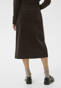 Brown corduroy midi skirt with a straight silhouette and subtle vertical ribbing, paired with black shoes and textured beige socks.