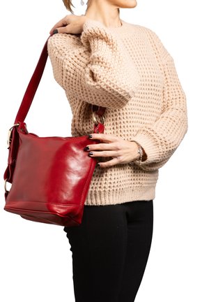 Borsa a tracolla rossa in pelle con texture liscia, forma quadrata e una ampia tracolla, tenuta da una persona che indossa un maglione beige a maglia.
