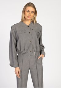 Grijze blazer met een kraag, twee borstzakken en gouden knopen. Heeft een geraffineerde tailleband en lange mouwen, gemaakt van een gestructureerde stof.