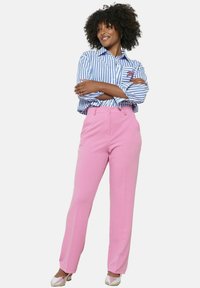 Roza hlače ravnih nogavic z gladko teksturo, oblečene z modro-belo prugasto srajco s detailom žepa.