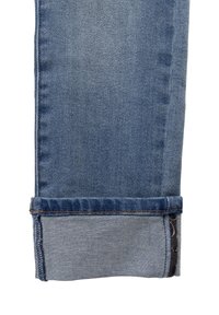 Jeans in denim blu con gamba affusolata, cuciture visibili e orlo cuffato con un motivo interno a contrasto.