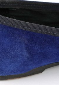 Gros plan d'une chaussure en daim bleu avec une bordure élastique noire et une semelle noire.