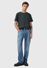 Dunkelgraues T-Shirt, lässige Passform, kombiniert mit hellblauen, distressed Jeans. Getragen mit einem schwarzen Gürtel und dunklen Schuhen, einfaches Design und Textur.