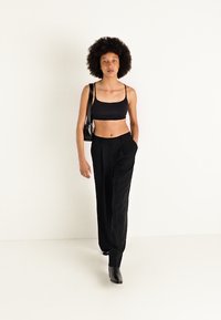 Crni cropped top i crne hlače visokog struka s vertikalnim naberanim detaljima, u kombinaciji s crnim gležnjačama i malom torbicom za rame.