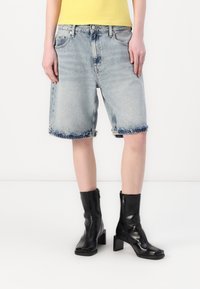 Lyseblå denimshorts med frayed kant, høy midje og fem-lomme design. Kombinert med svarte hæler og en gul t-skjorte.