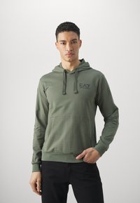 Felpa verde oliva con tasca a marsupio, cordini regolabili e logo EA7 sul petto. Tessuto morbido e leggero con polsini a costine.