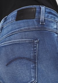 Vaqueros de denim con efecto stone-wash que presentan una etiqueta de cuero oscuro en la cintura, detalles de costura sutiles y un diseño estándar de bolsillo trasero.