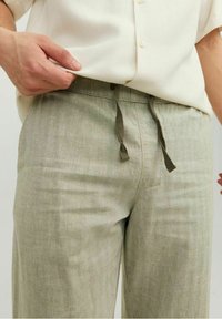 Ljusgröna linnebyxor med en slät textur, dragsko i midjan och detalj på framfickan. Bärs med en off-white skjorta.