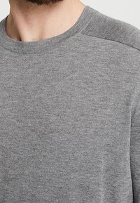 Grå sweatshirt med rund hals och subtila texturerade axeldetaljer, tillverkad av mjukt, stickat tyg, som framhäver den sömlösa designen.