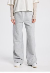 Pantalon de survêtement gris à jambes larges en tissu doux, avec une coupe décontractée et une texture subtile, associé à des baskets blanches.
