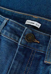 Jeans in denim blu con bottone in ottone che presenta la scritta "TWO SOON JEANS." L'etichetta riporta "TWO SOON" e la taglia "28/32." I punti di cucitura sono in beige a contrasto.