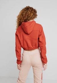 Beskuren, huva sweatshirt i rostorange med ribbad infällning och elastisk midja, i kombination med ljusrosa sweatpants med elastisk midja.